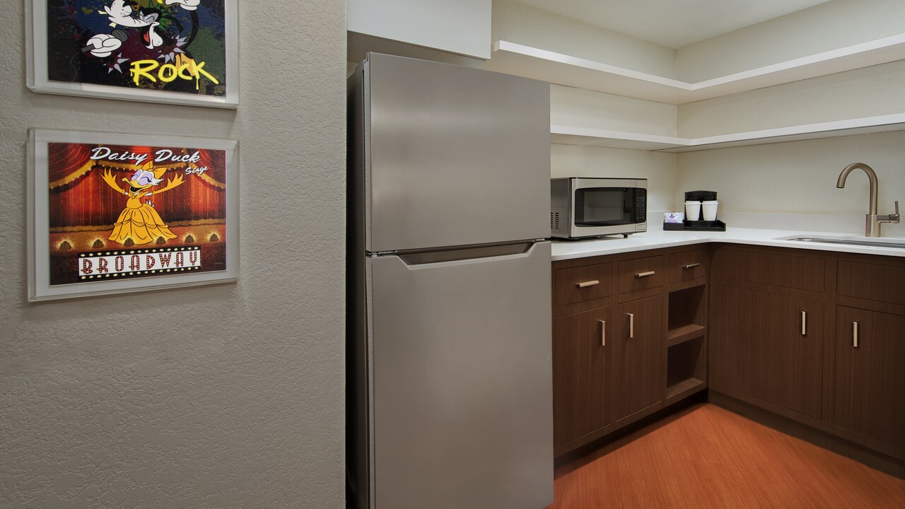 Framed Disney character artwork, refrigerator next to a microwave, coffee maker and sink