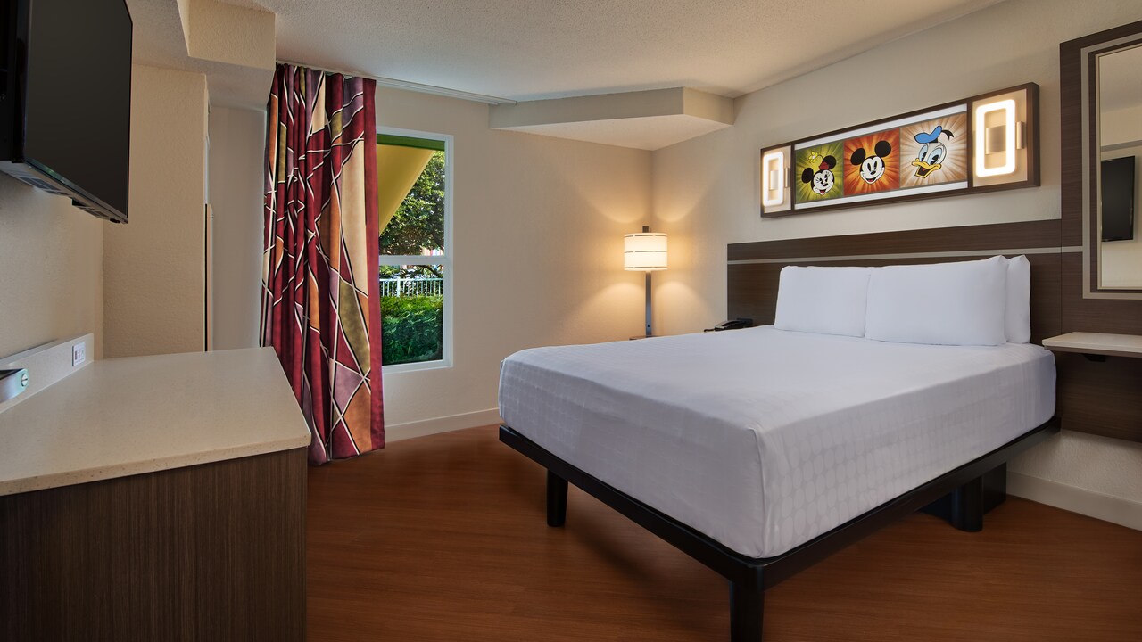 Bed, floor lamp and framed Disney character art above headboard on wall