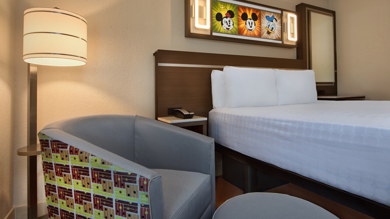 Chair, ottoman, floor lamp, end table, bed, mirror and framed Disney character art on wall above bed