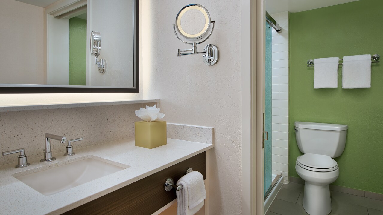 Bathroom sink, towel, mirror, toilet and small round mirror on wall
