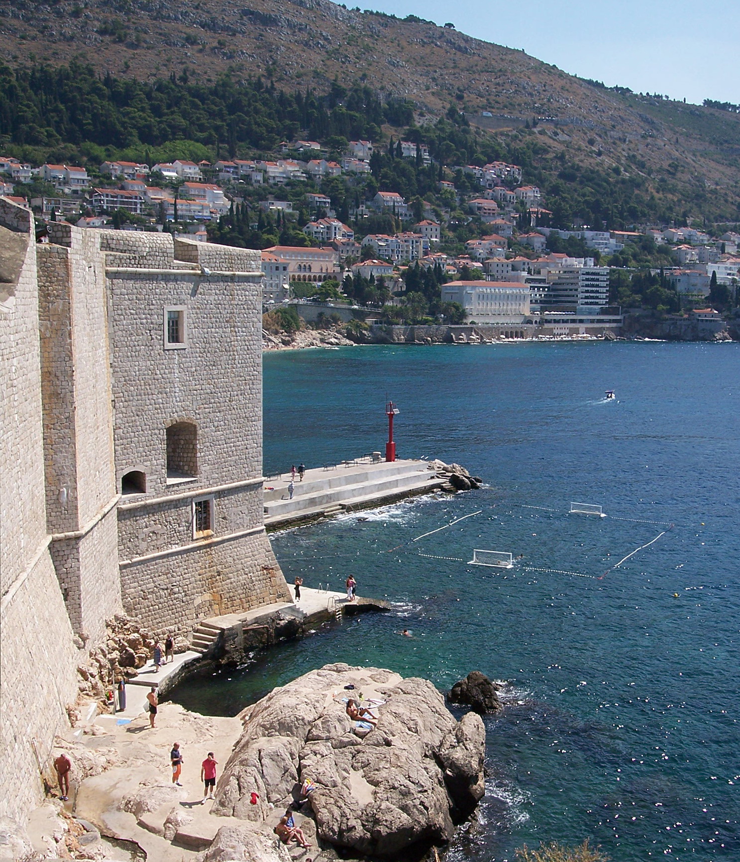 Stone sea wall beside Dubrovnik's old harbor, with a red navigation light and the bay