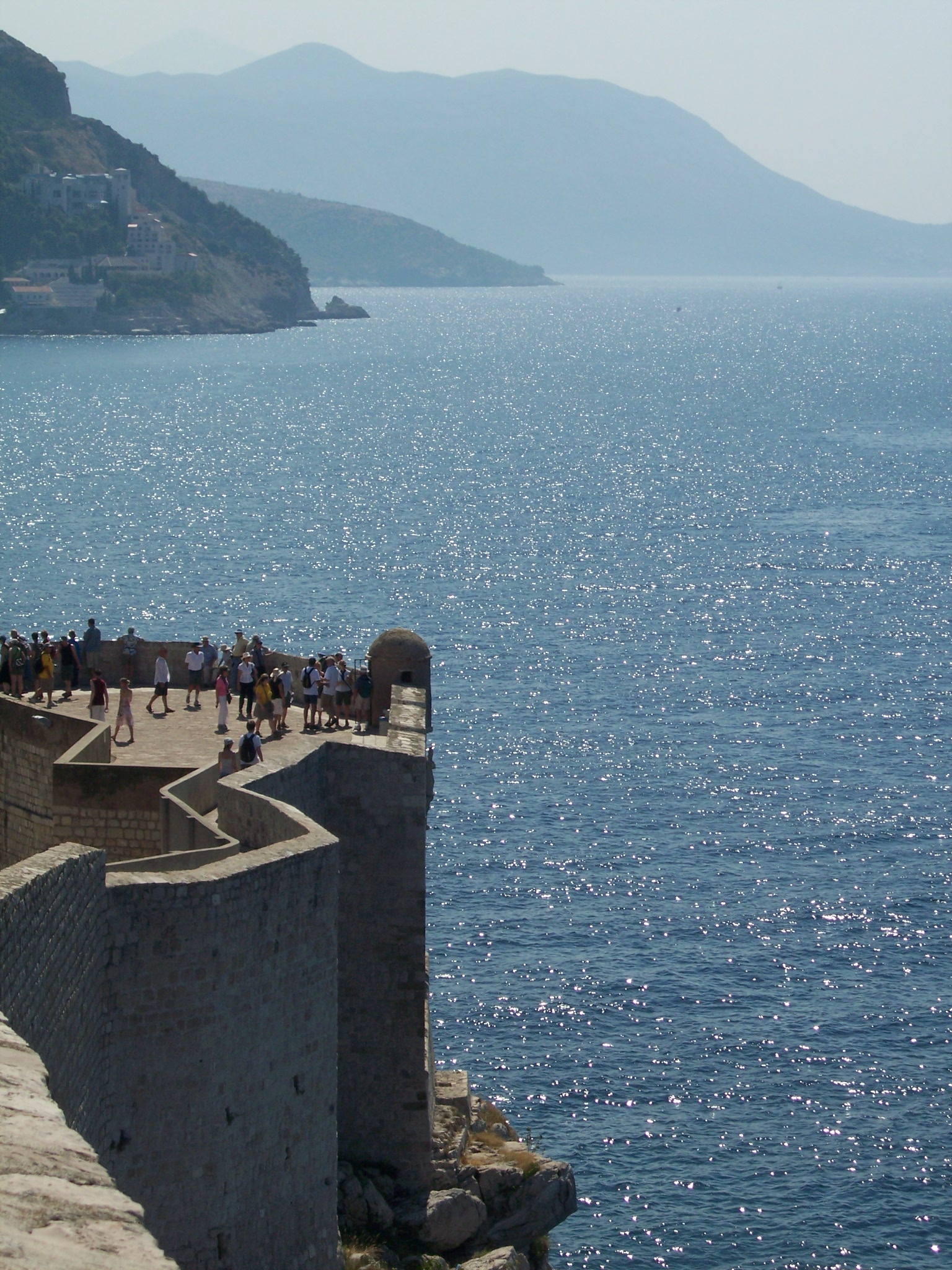 Visitors on a stone rampart of the Dubrovnik walls, with the sea beyond