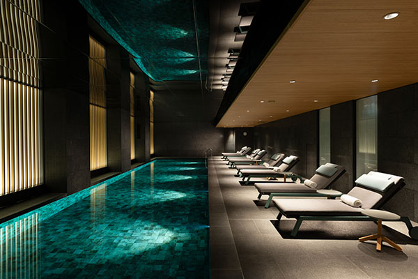 Indoor pool with teal water, a row of lounge chairs, and wood slats along the left wall