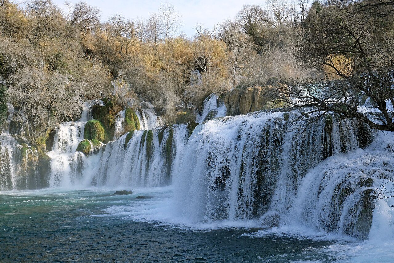 Close view of Skradinski Buk, with water pouring over mossy limestone into a turquoise pool