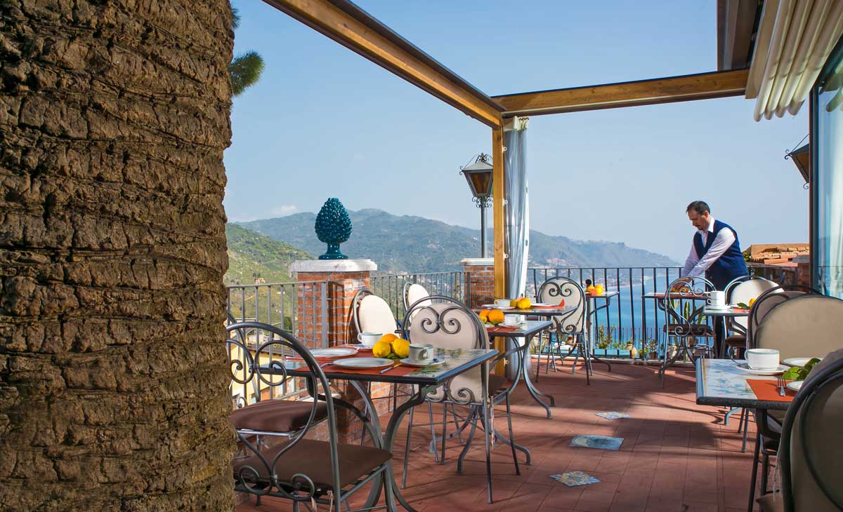 Breakfast terrace with set tables overlooking the bay and mountains