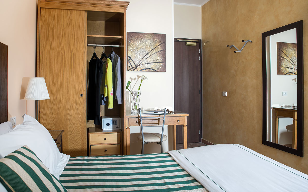 Double room without a view, with a bed, open wardrobe, safe, and desk