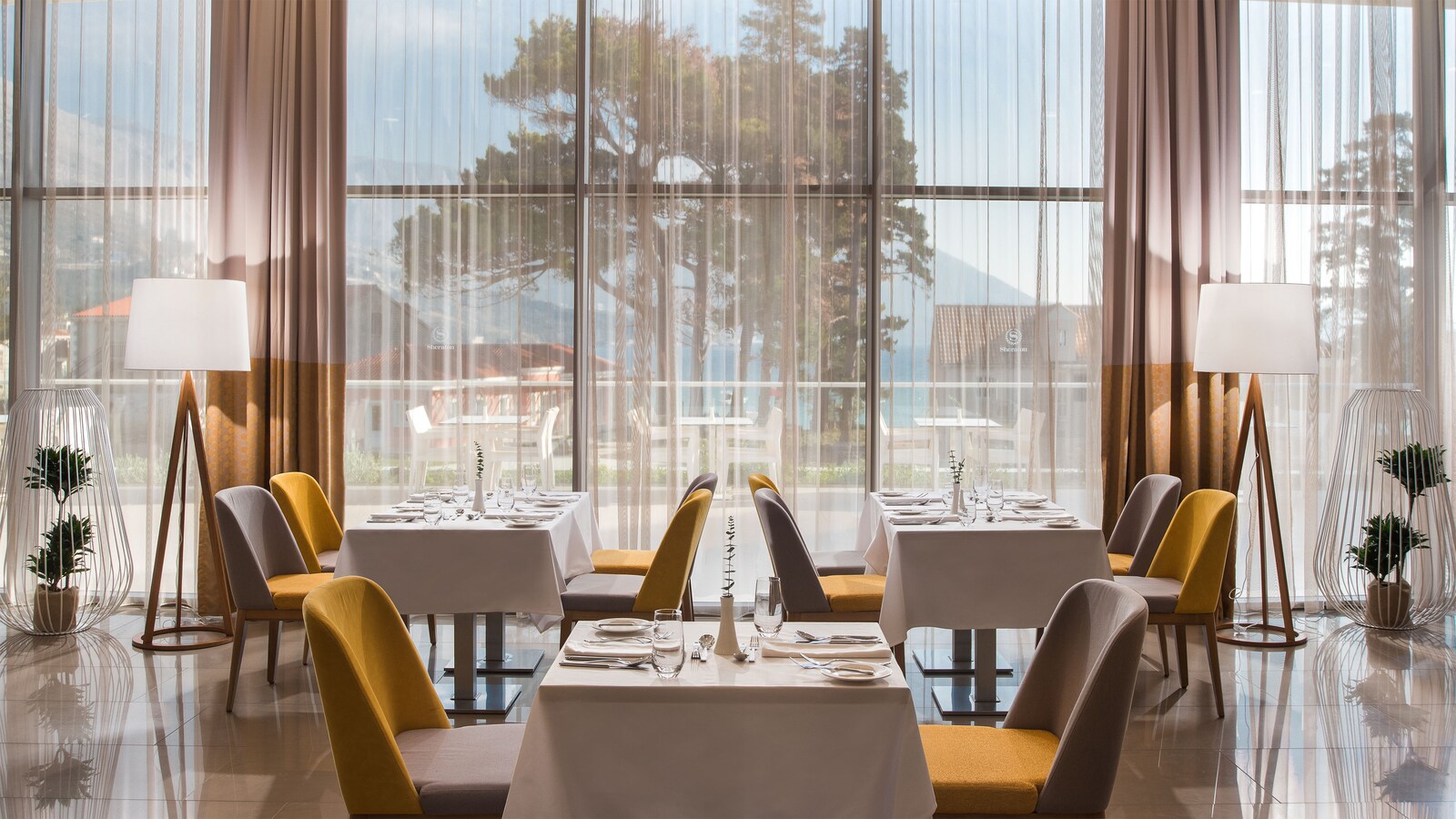 Leut restaurant, with set tables and sheer curtains toward the trees and the sea