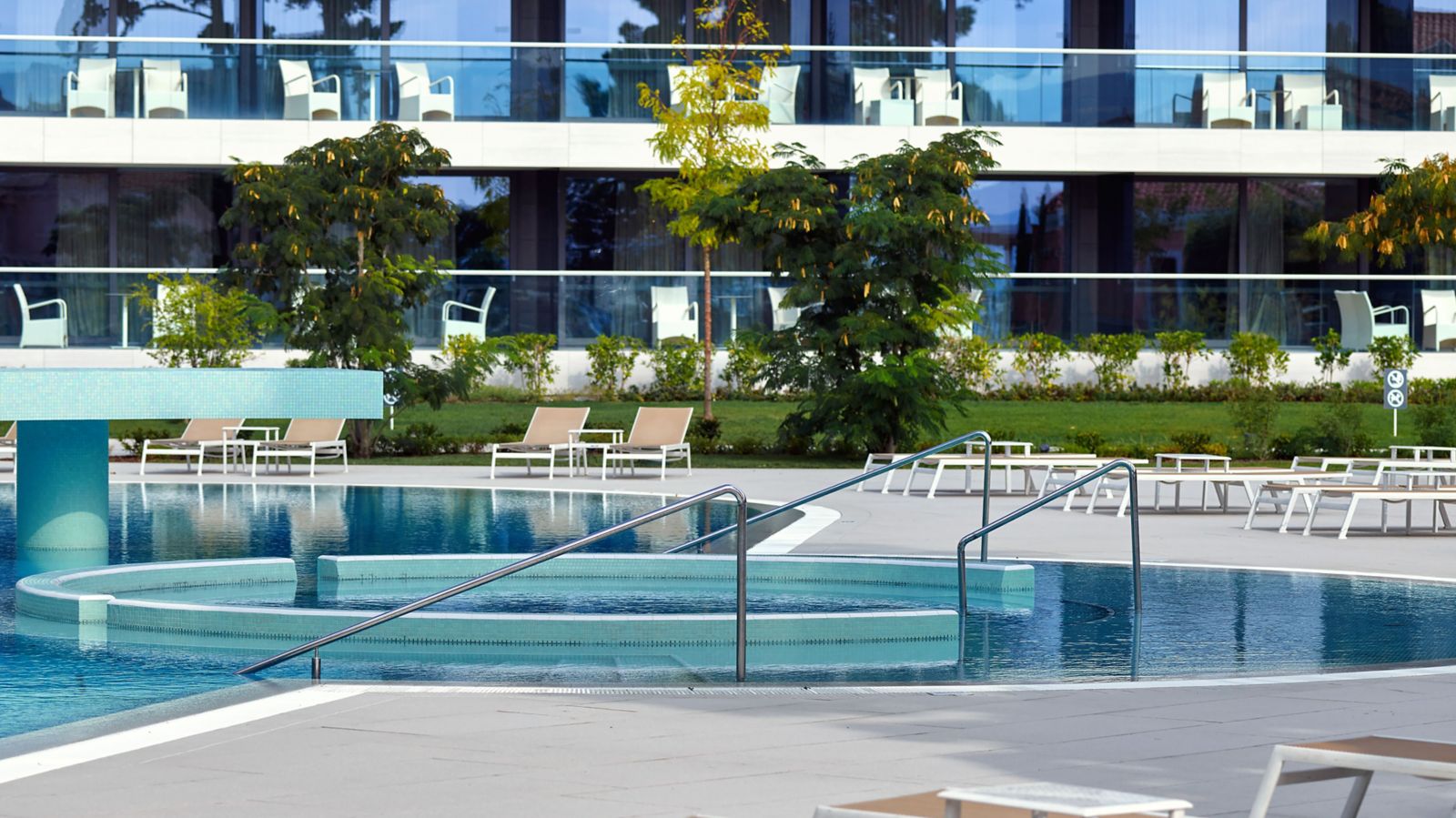 Outdoor pool with a round tiled step, lounge chairs, and the hotel balconies behind it