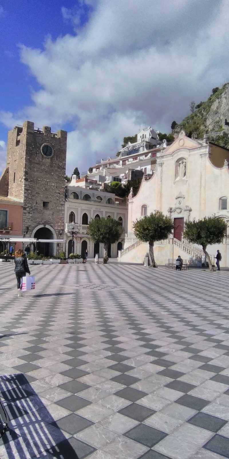 Piazza IX Aprile in Taormina, a checkerboard square with a stone clock tower and a baroque church