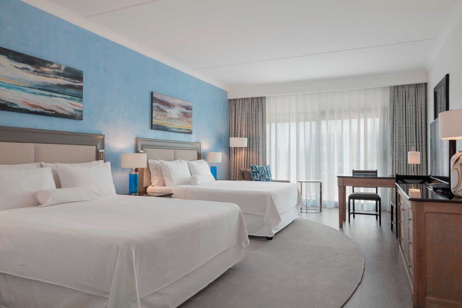Deluxe guest room with two queen beds, a desk, and sheer curtains