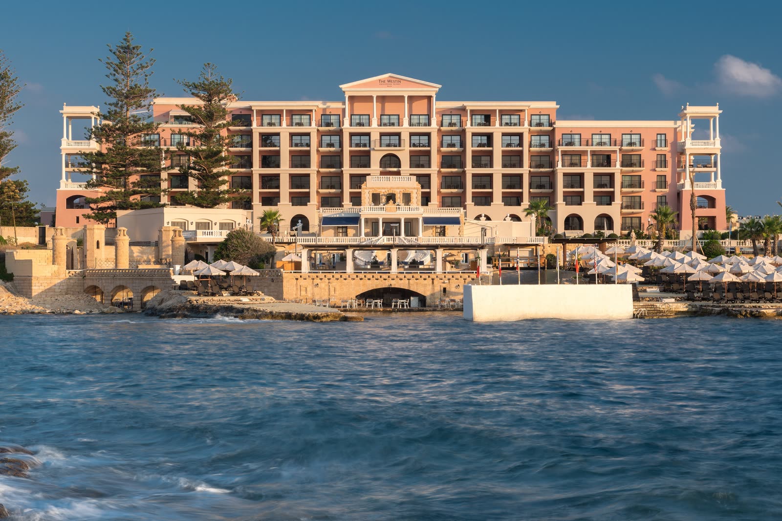 The Westin Dragonara seafront, with the hotel name on the facade and umbrellas along the water