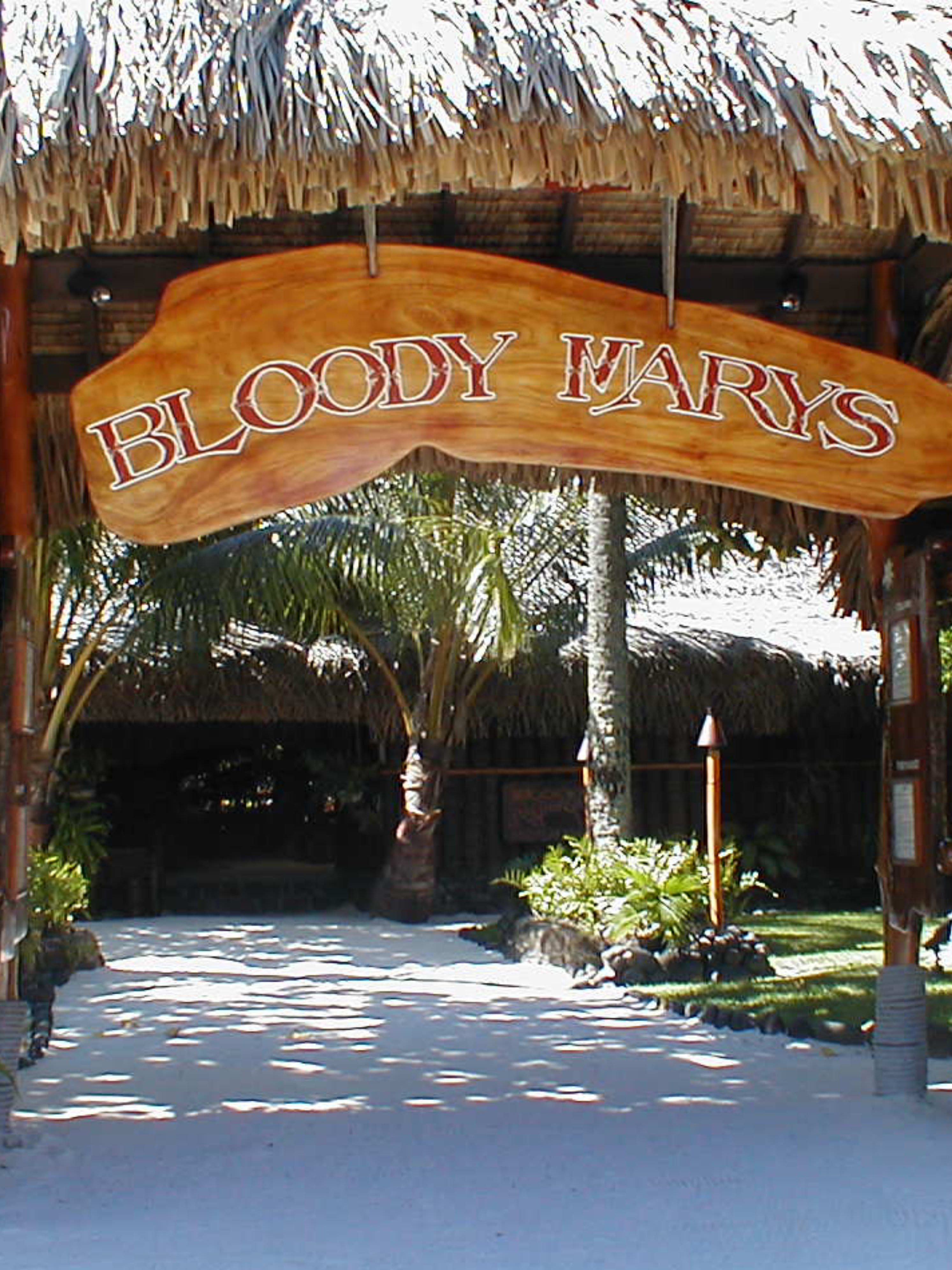 Bloody Mary's Restaurant entrance in Bora Bora with carved wooden sign, thatched roof and white sand path